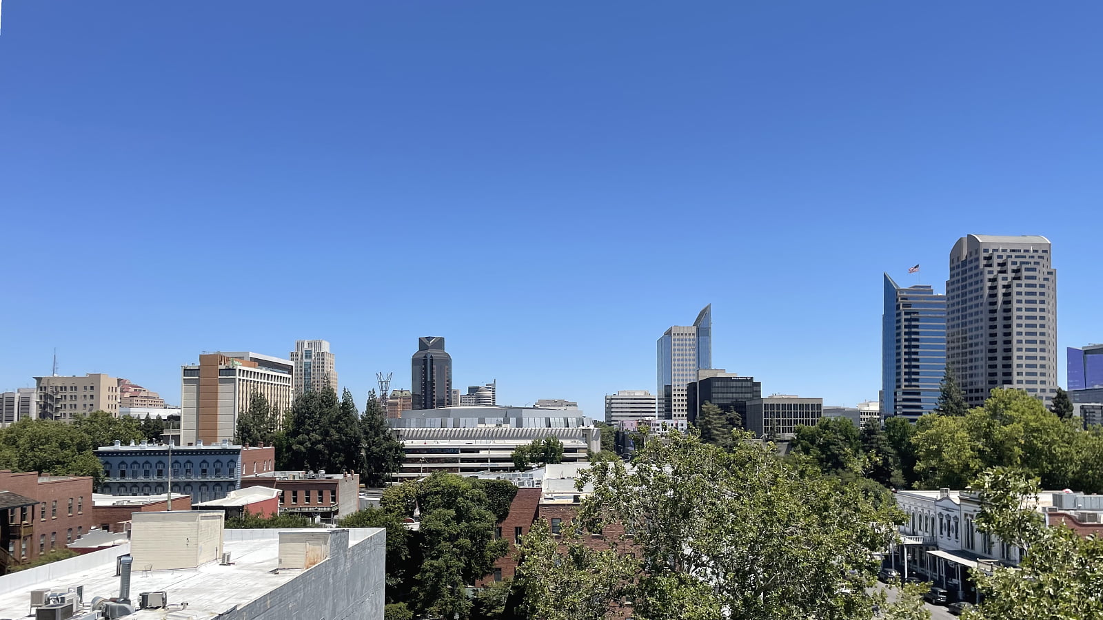 Downtown Sacramento skyline with modern office buildings and tree-lined streets under a clear blue sky